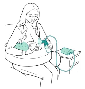 Parent sitting to breastfeed baby on one breast and pump milk on the other breast. 