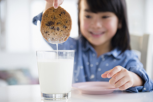 Young girl dunking cookie in glass of milk.
