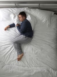 Person sleeping in bed, using pillows to keep spine aligned.